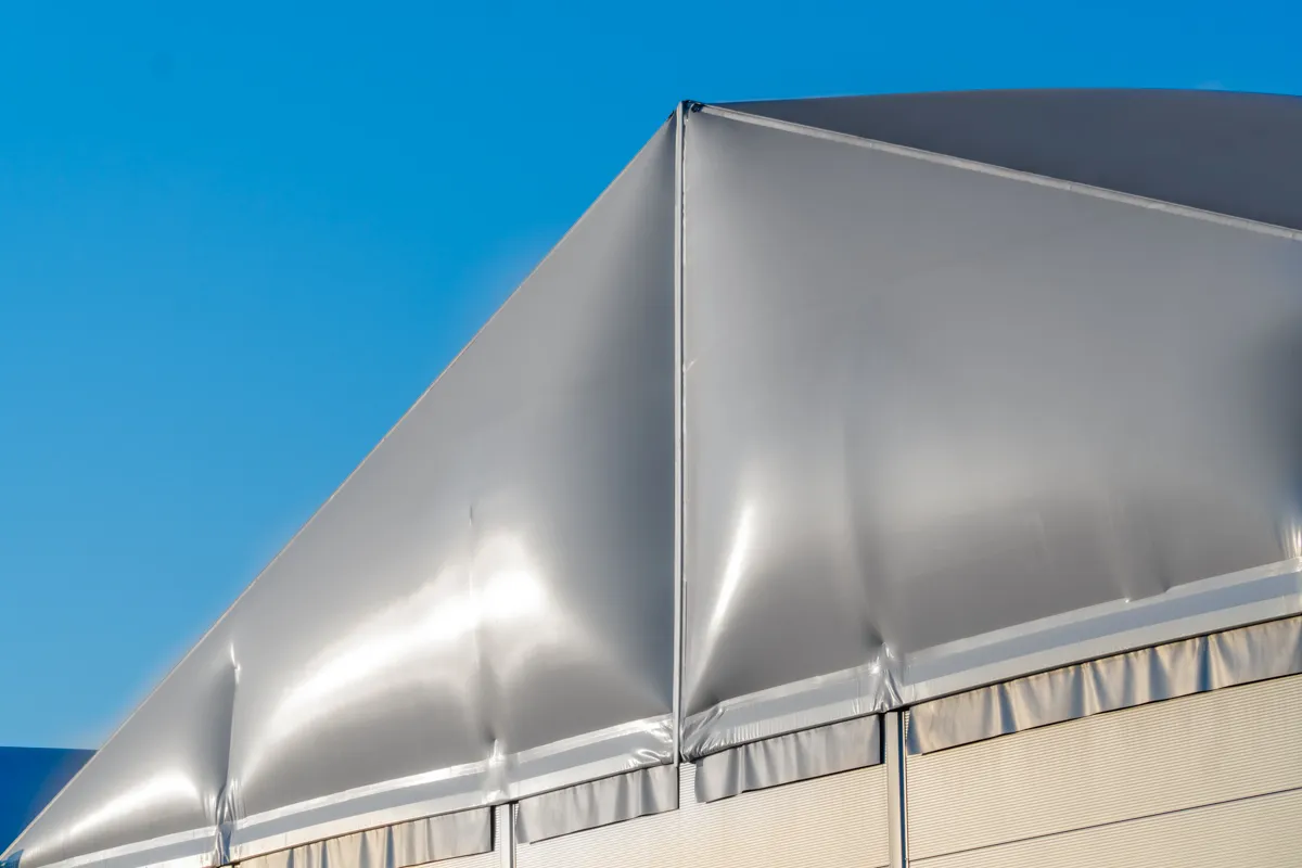 Silbergraue Dachplane einer Reithalle vor blauem Himmel